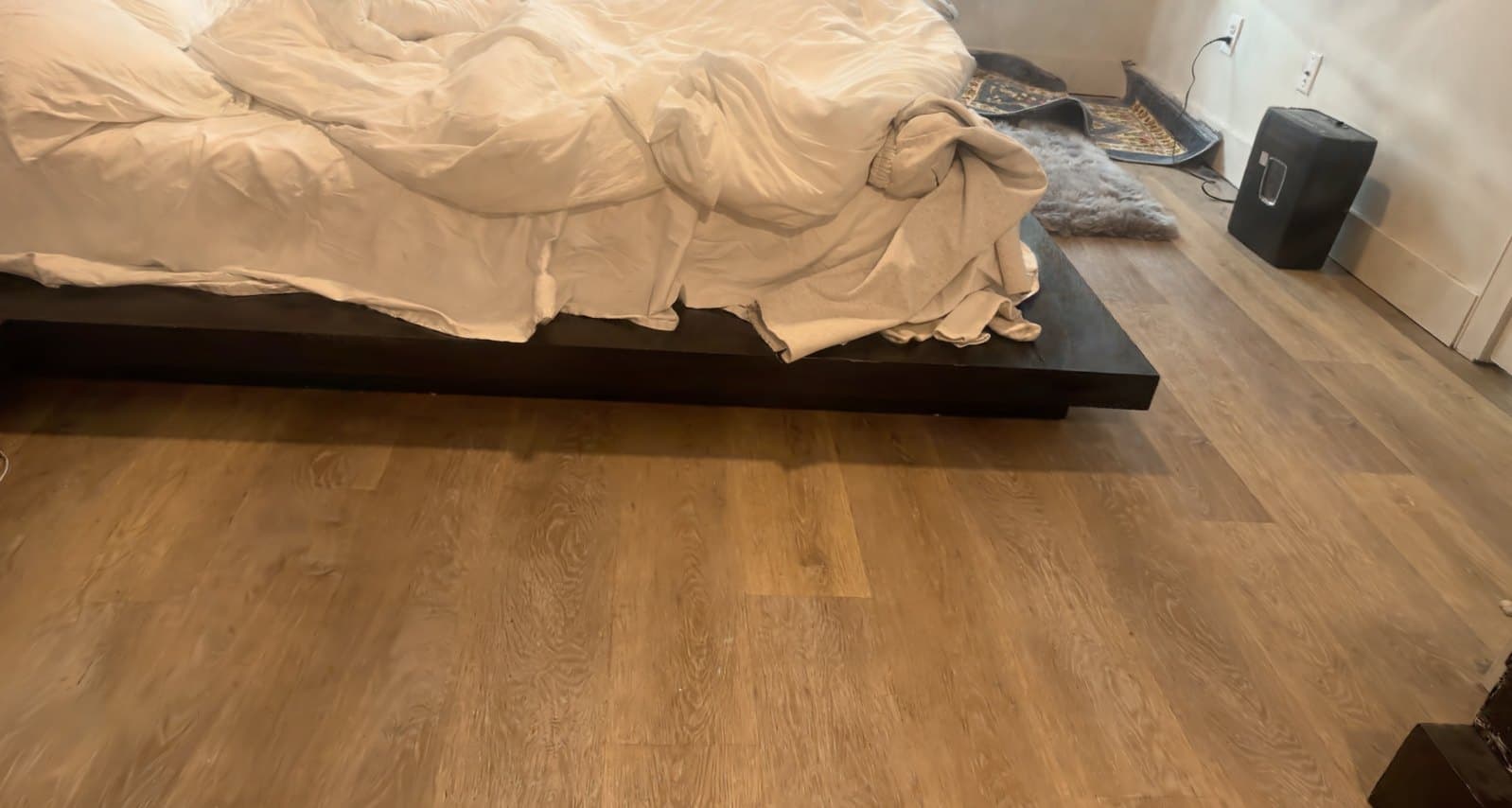 Bedroom reconstructed as a Gaussian splat: an unmade bed on a dark platform frame beside a wide oak floor.